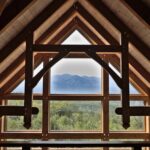 Rustic wooden interior showcasing timber trusses with a stunning mountain view through large windows.