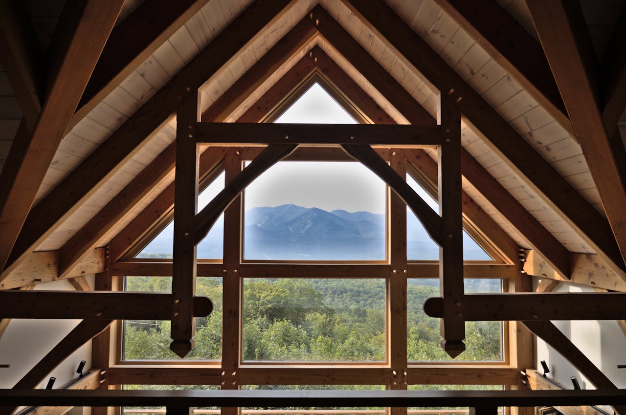Rustic wooden interior showcasing timber trusses with a stunning mountain view through large windows.